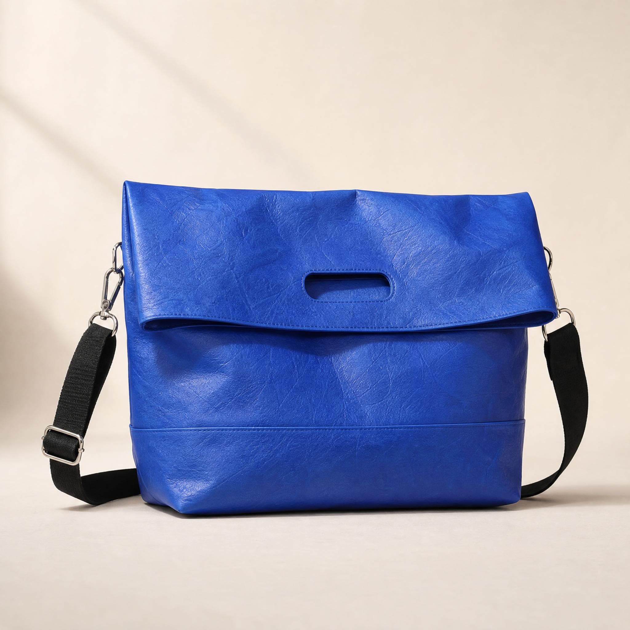 Blue crinkled fold-over messenger bag, front view on a beige background
