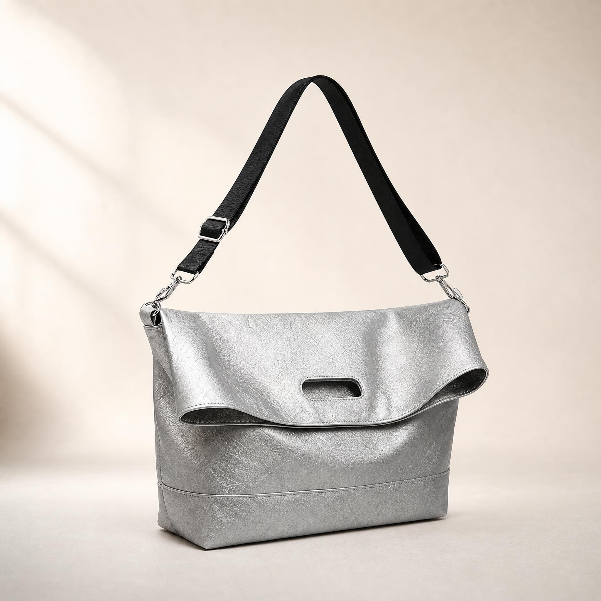 Metallic silver crinkled fold-over messenger bag, front view on a seamless beige background